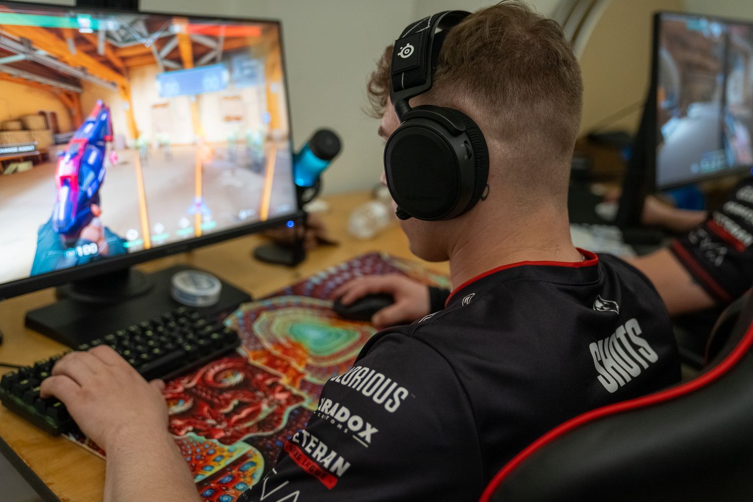 Gamer wearing headphones plays at gaming setup with RGB keyboard and monitor in dark room.