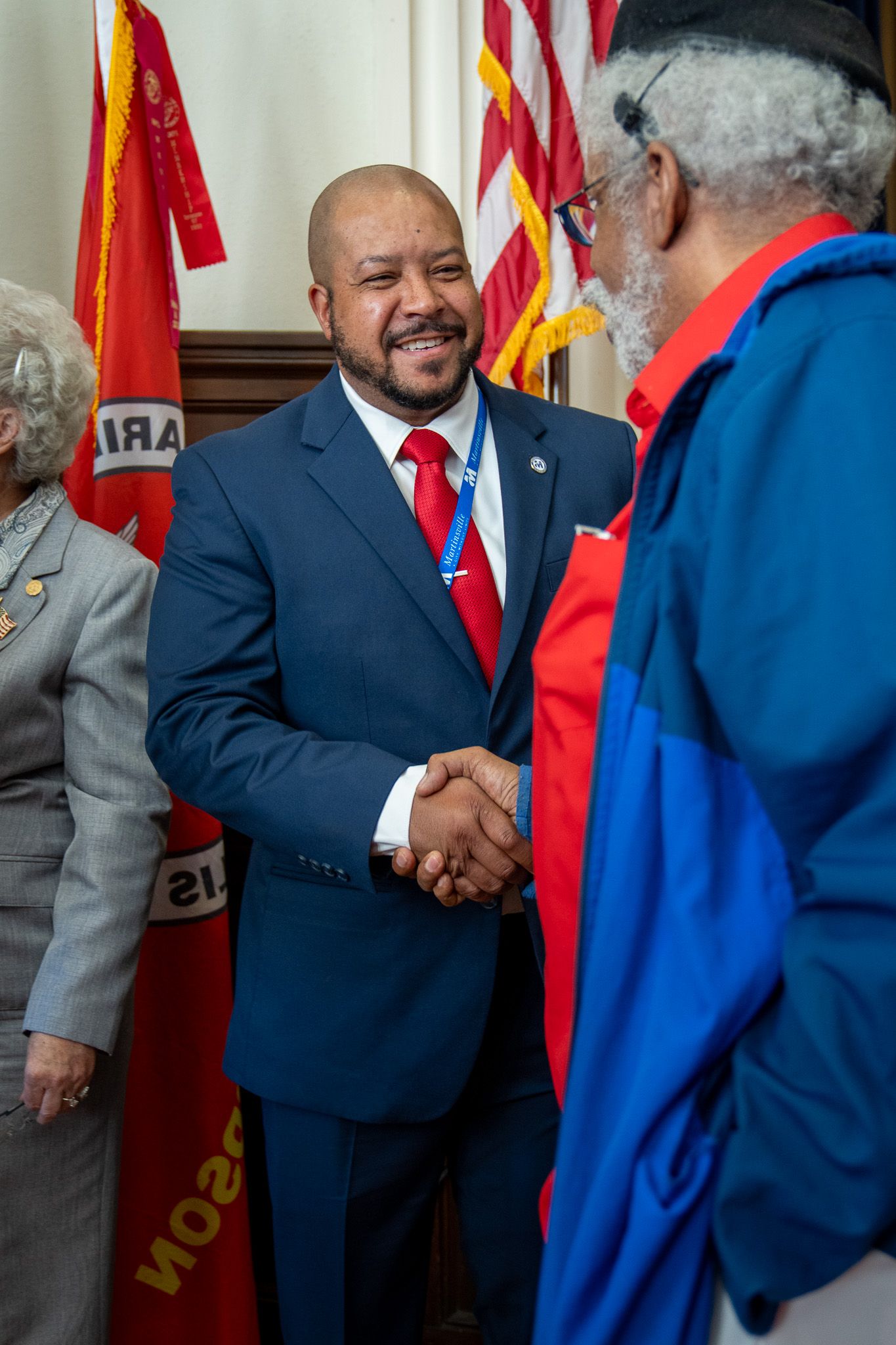 Professional greeting and handshake between two individuals at formal event with American flag in background.