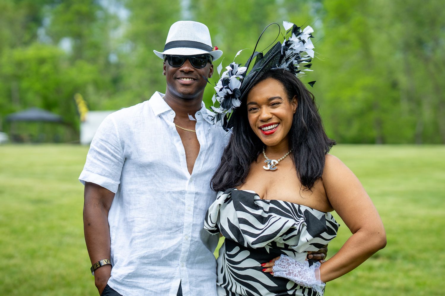 A couple in summer attire stands together on a grassy lawn, wearing coordinated black and white outfits.