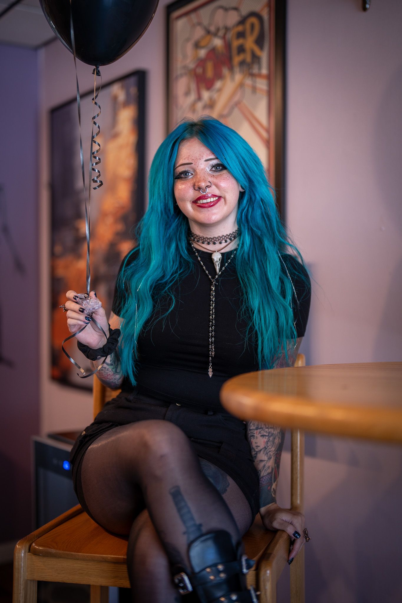 Alternative style portrait featuring vibrant teal hair, black outfit, and balloon in moody indoor setting.
