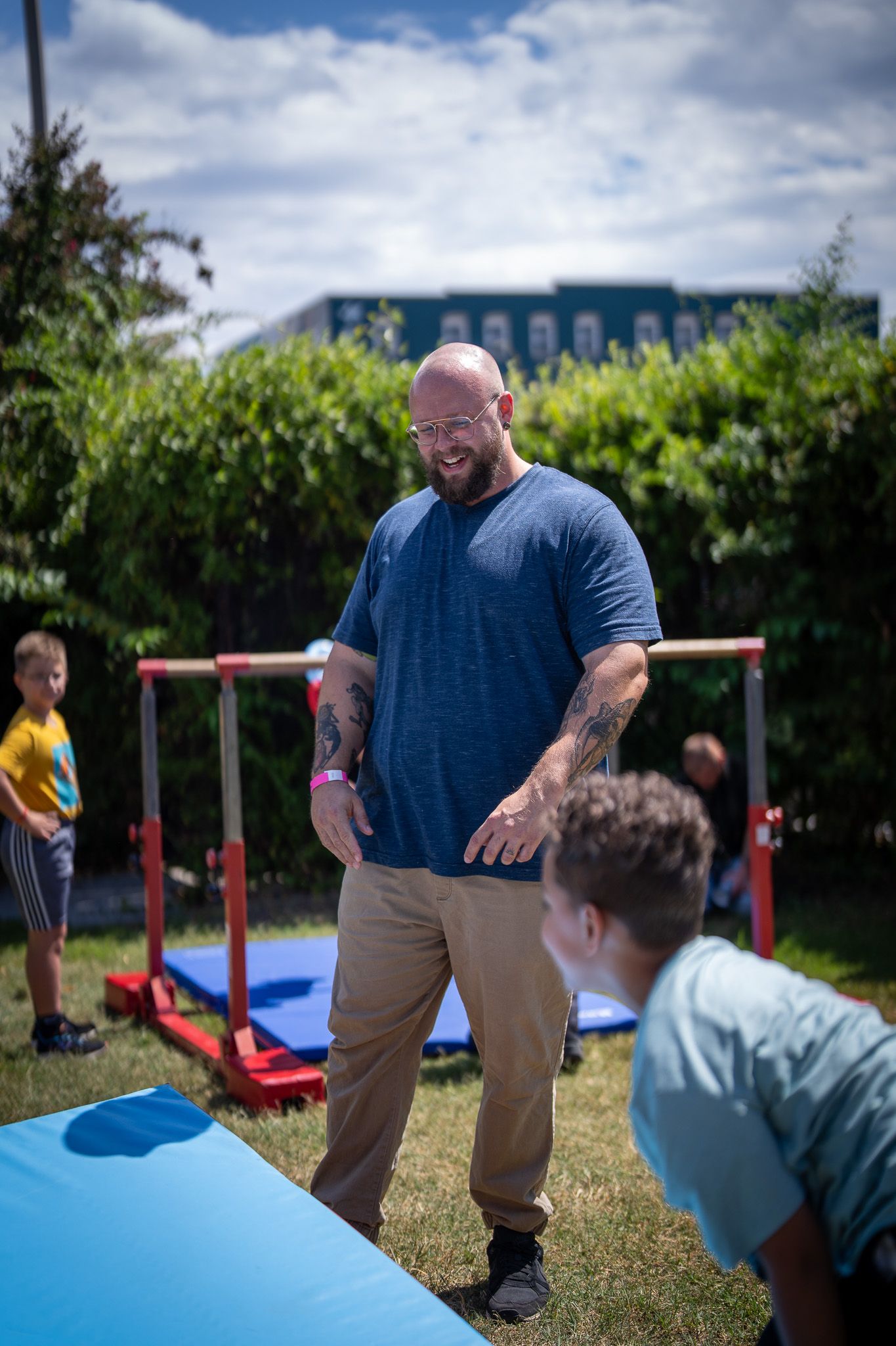 Person in a blue t-shirt and khakis smiling while interacting with others in a backyard playground area.