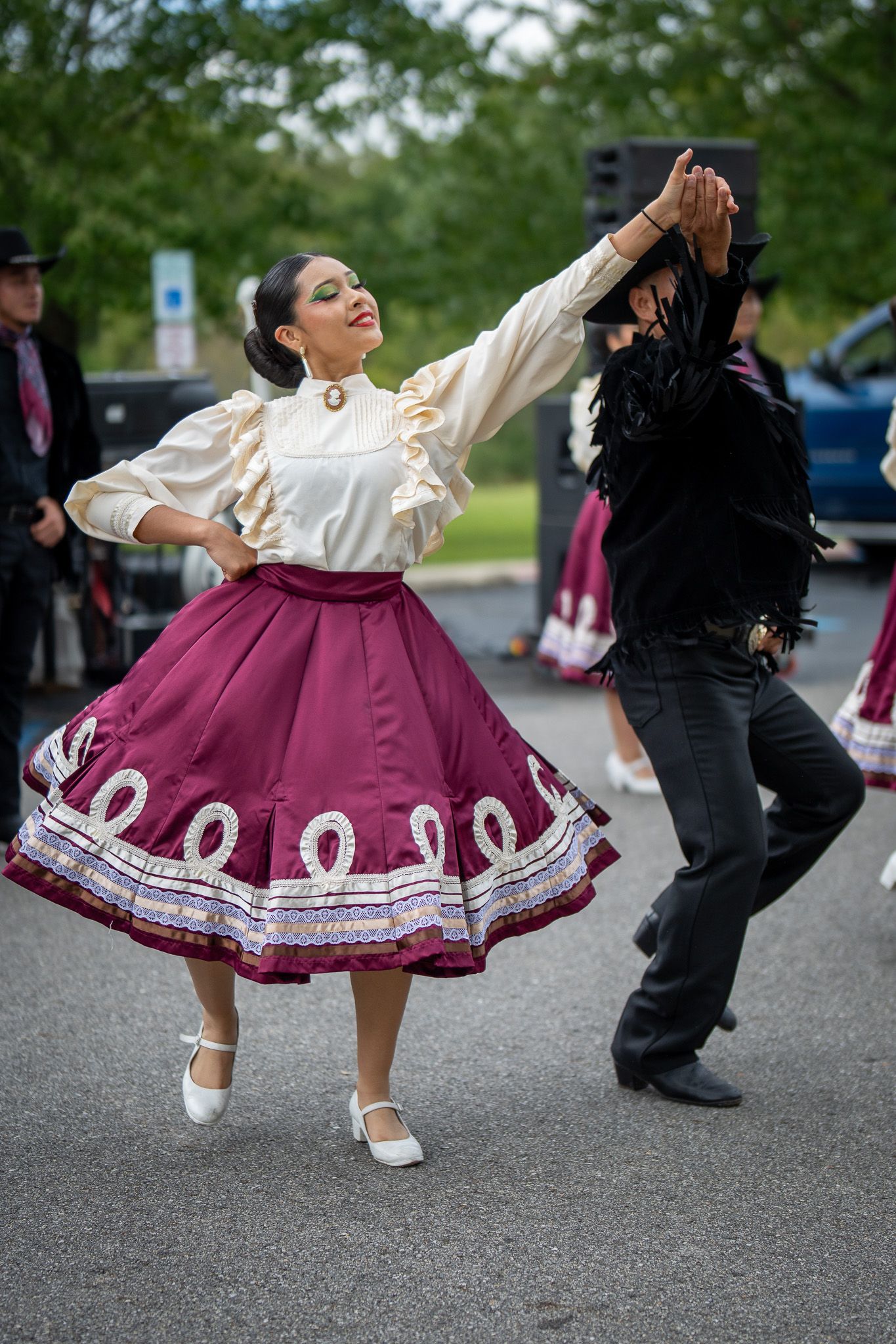 Traditional dancers in burgundy skirts and white tops performing folk dances on pavement.