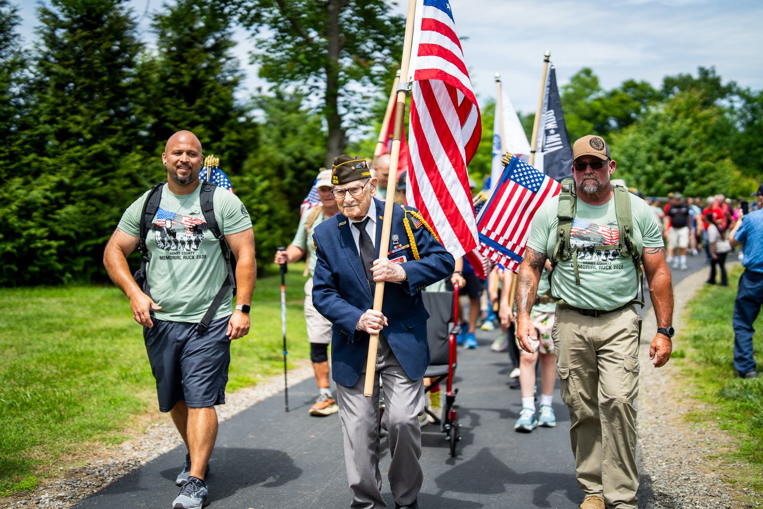 Veterans and supporters march together on a trail carrying American flags during a patriotic event.