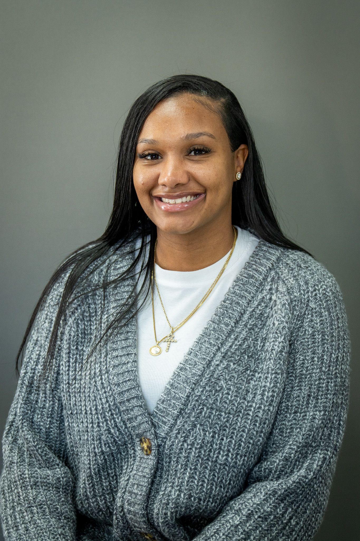 Professional portrait of someone wearing a gray knit cardigan over a white top with a necklace against a neutral background.