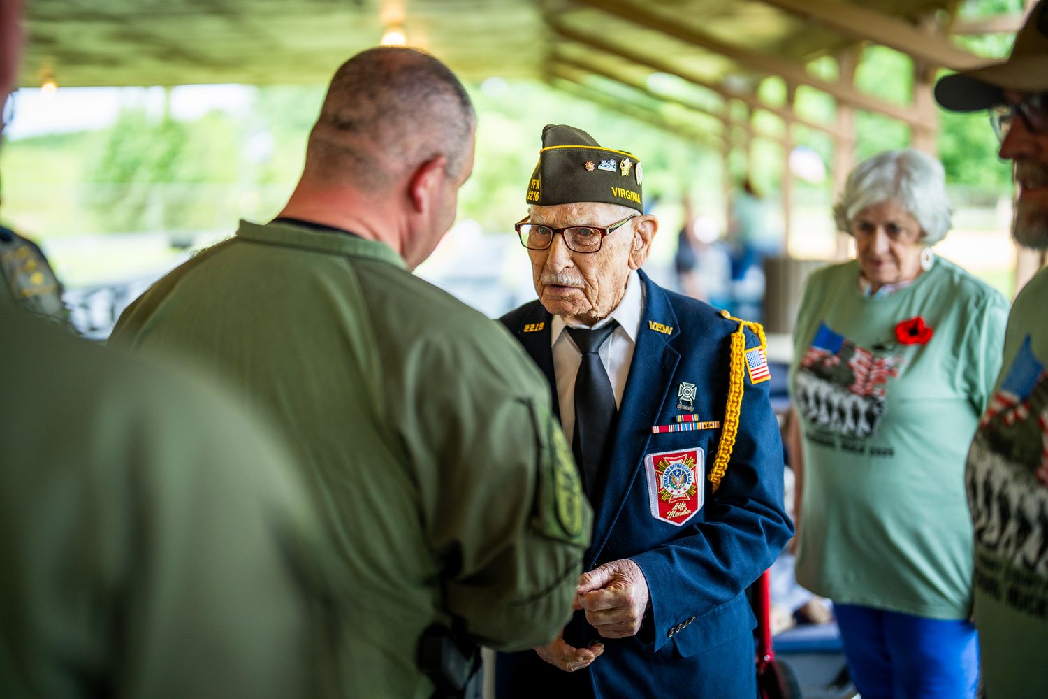 Veteran in dress uniform speaking with another participant during a military recognition ceremony.