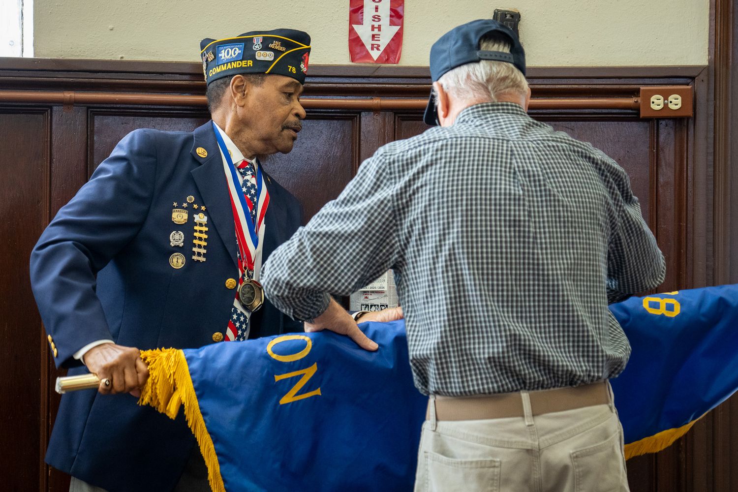 Two veterans in military attire chat during an event while holding blue service banners.