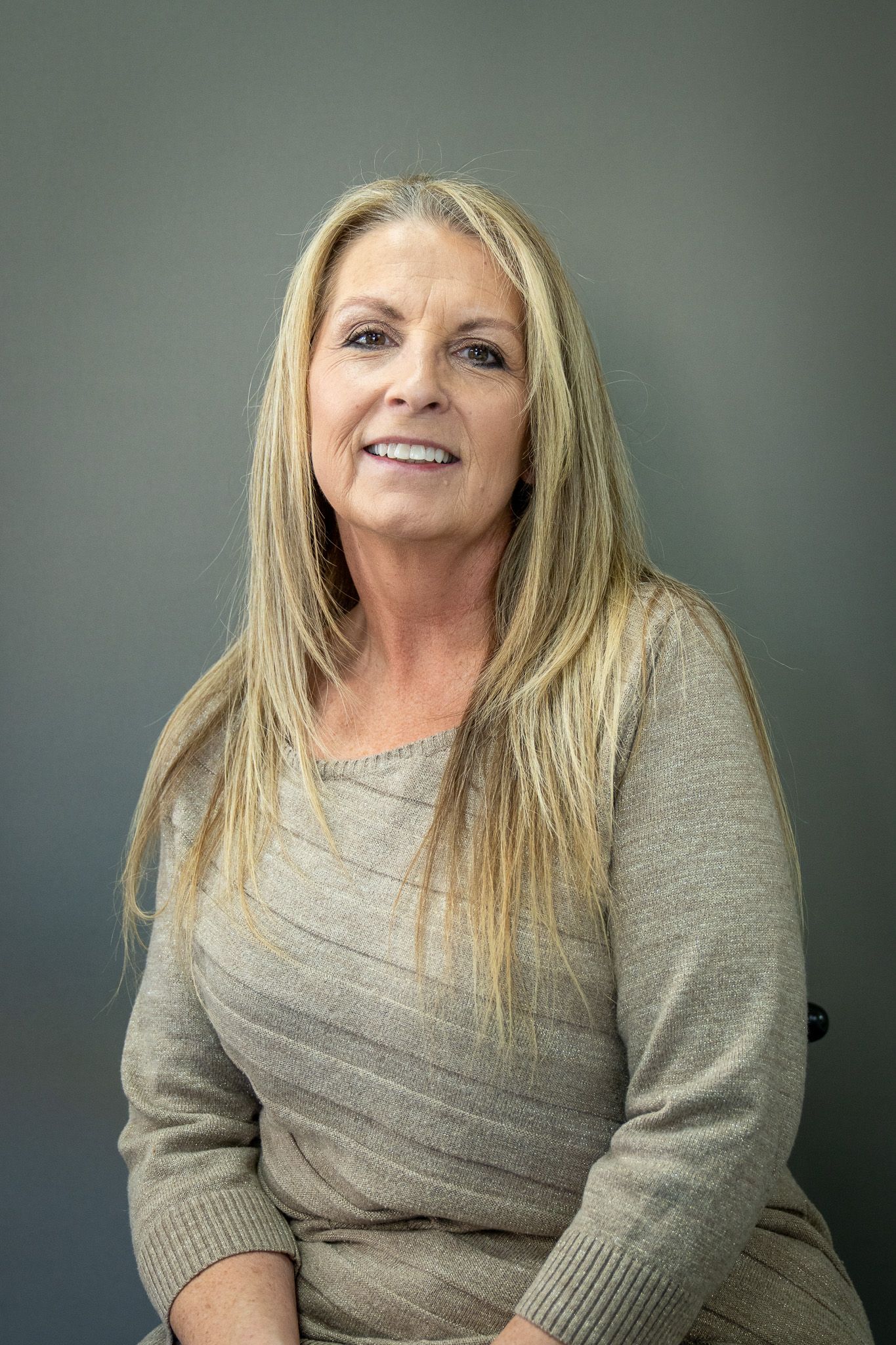 Portrait of a woman in a gray sweater against a dark backdrop.