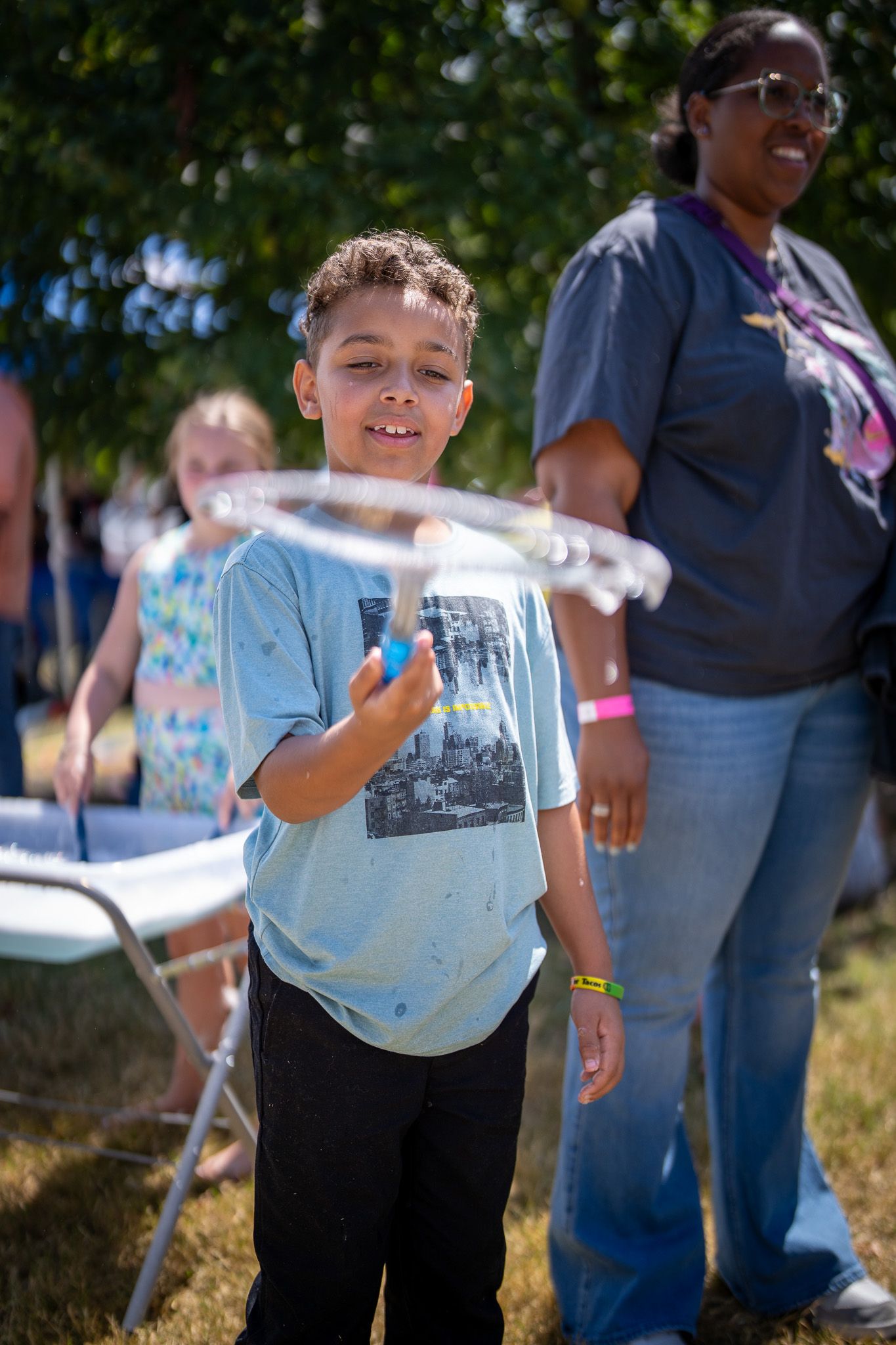 Young person in light blue t-shirt smiles while playing with water outdoors on a sunny day.