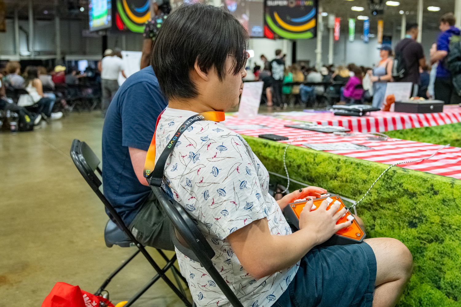 Person playing a video game handheld while sitting in a folding chair at a community gathering.