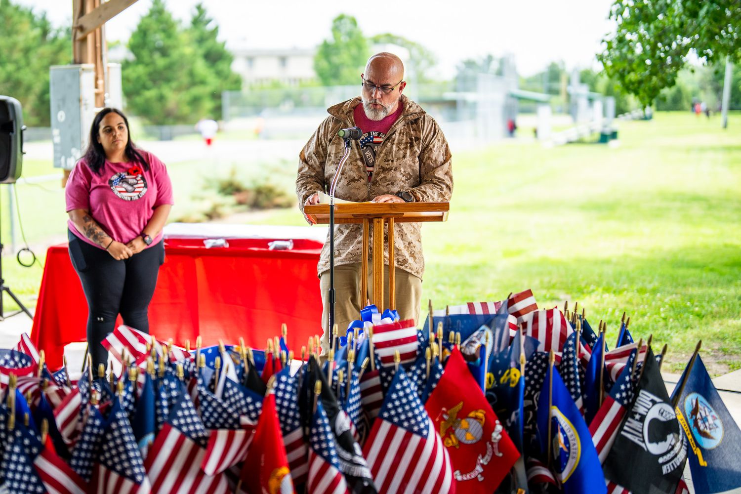 Military-themed outdoor gathering with display of American flags and military service branch flags.