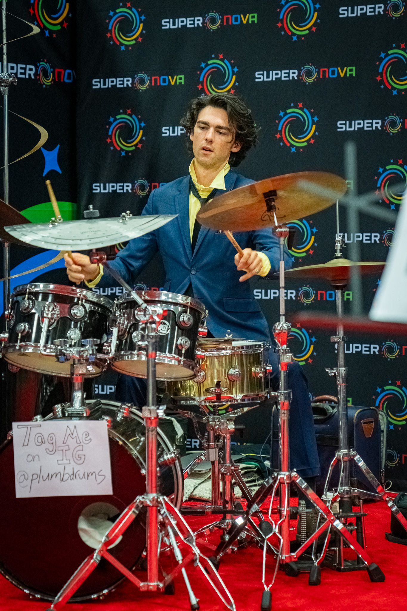 Professional drum kit setup with red hardware against dark backdrop at music event.