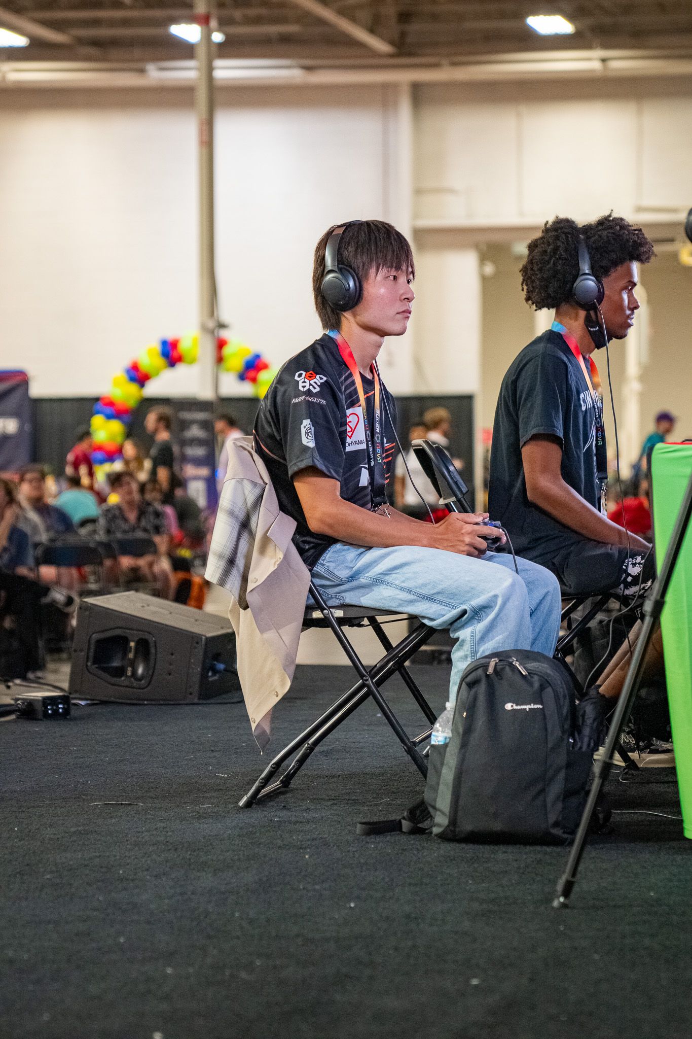Esports players wearing headsets compete at a gaming tournament with colorful balloon arch visible in background.