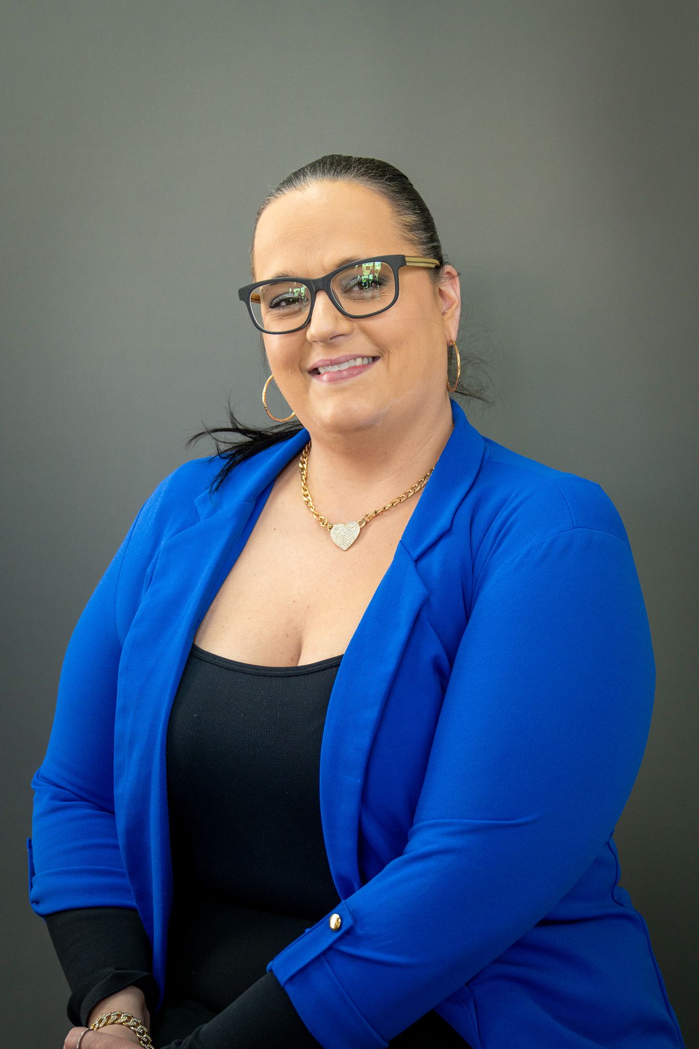 Professional portrait of someone in a royal blue blazer and glasses smiling against a neutral backdrop.
