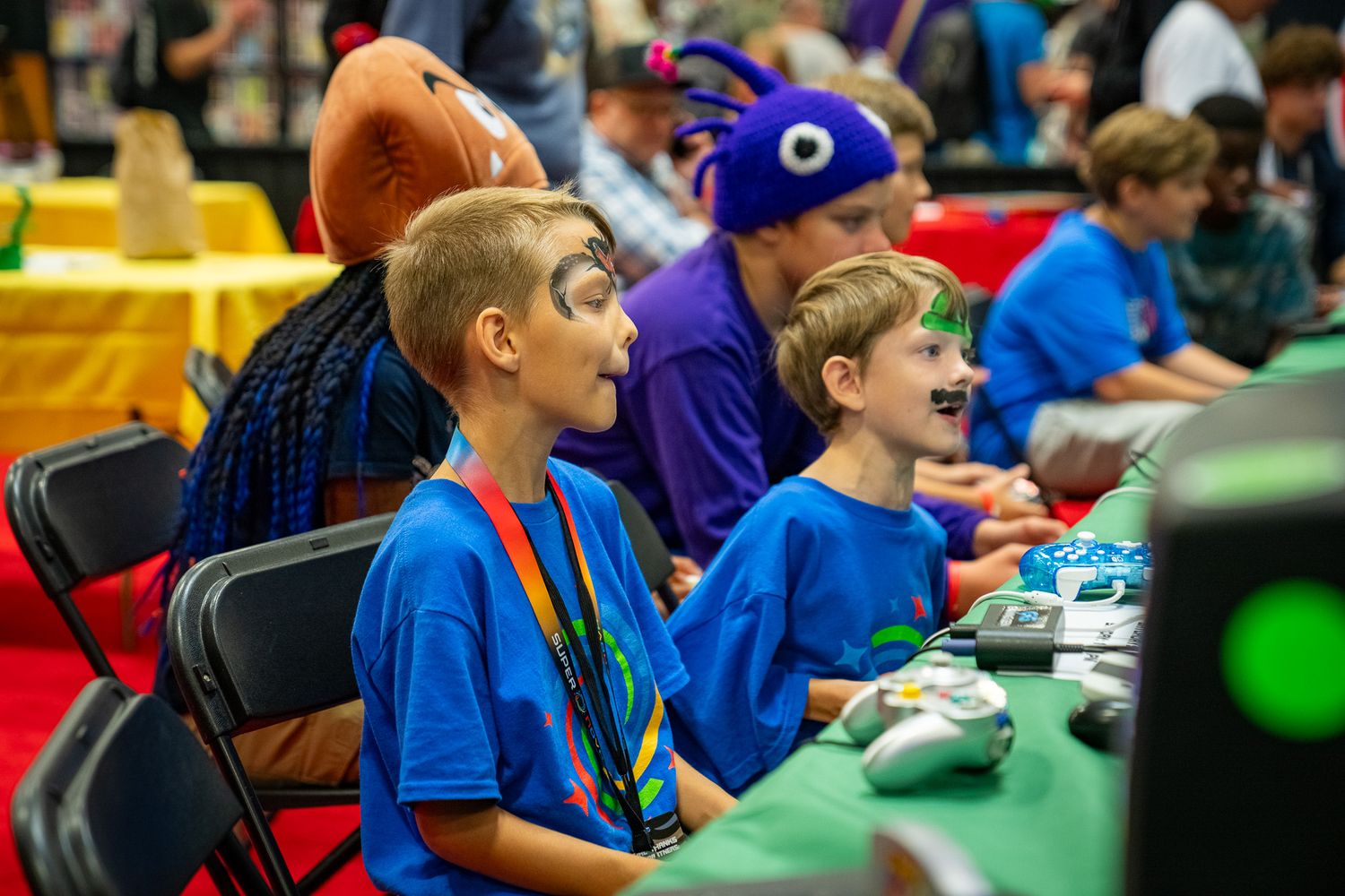 Young participants in blue shirts compete at an esports gaming event with monitors and controllers.