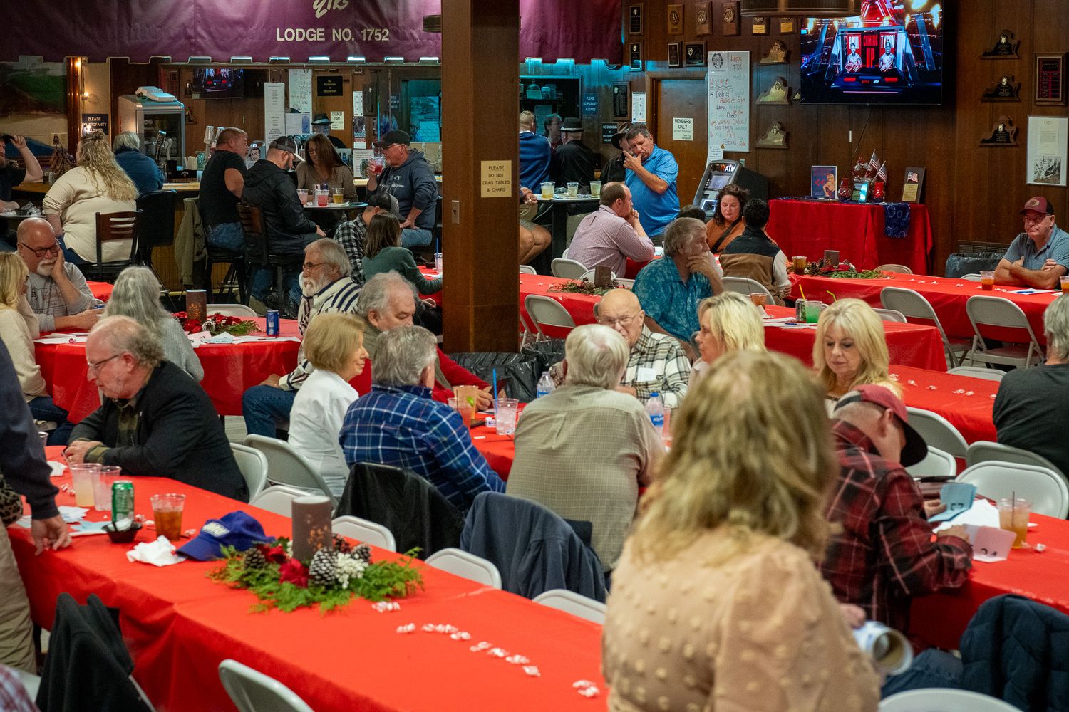 People gather at tables with red tablecloths in a large dining hall for a social event or celebration.