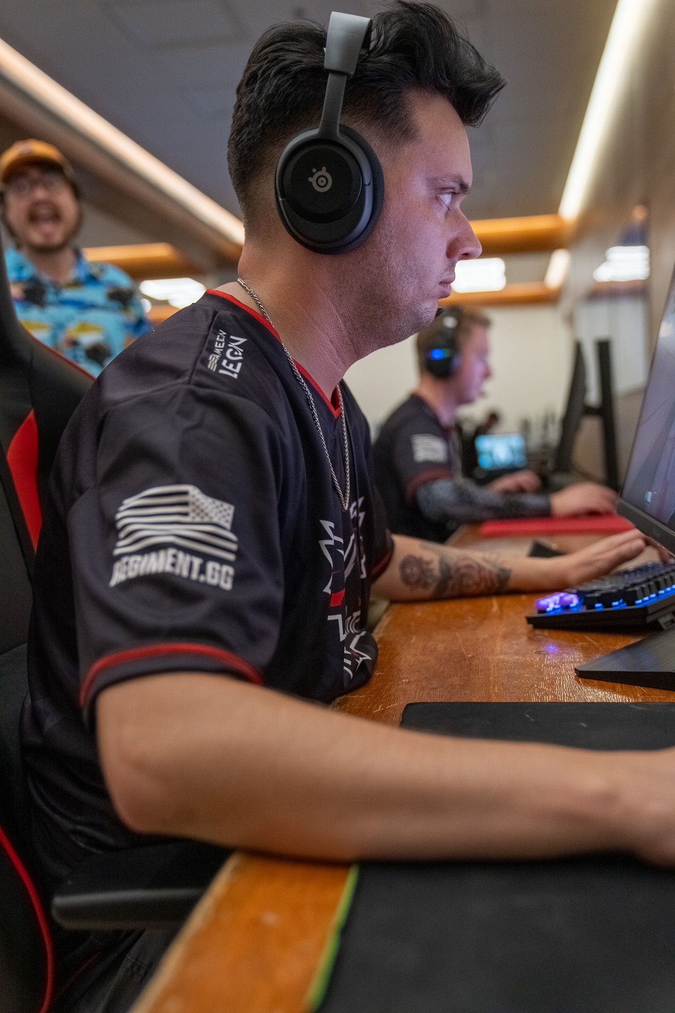 Professional esports players wearing headsets focus intently during competitive gaming tournament at wooden tables.