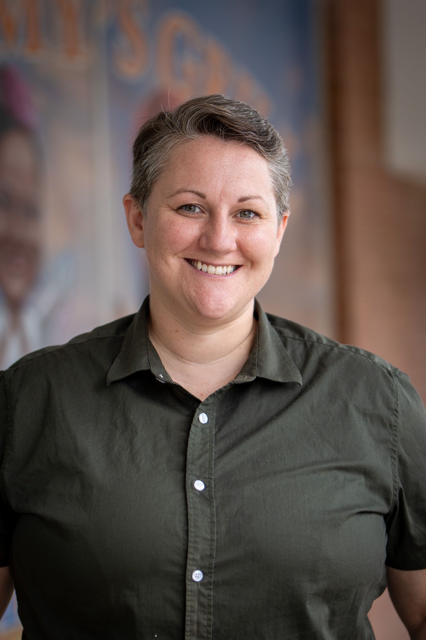 Professional headshot of someone wearing an olive green button-down shirt smiling warmly at the camera.