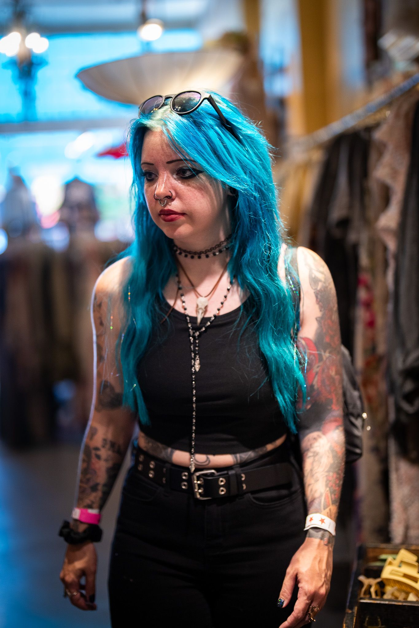 Alternative style portrait showing bright blue hair, tattoos, dark clothing and choker necklace in indoor retail setting.