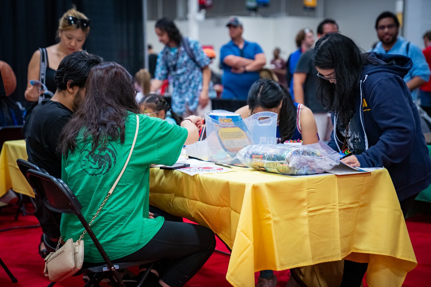 People seated at tables covered in yellow tablecloths at a large indoor event or convention.
