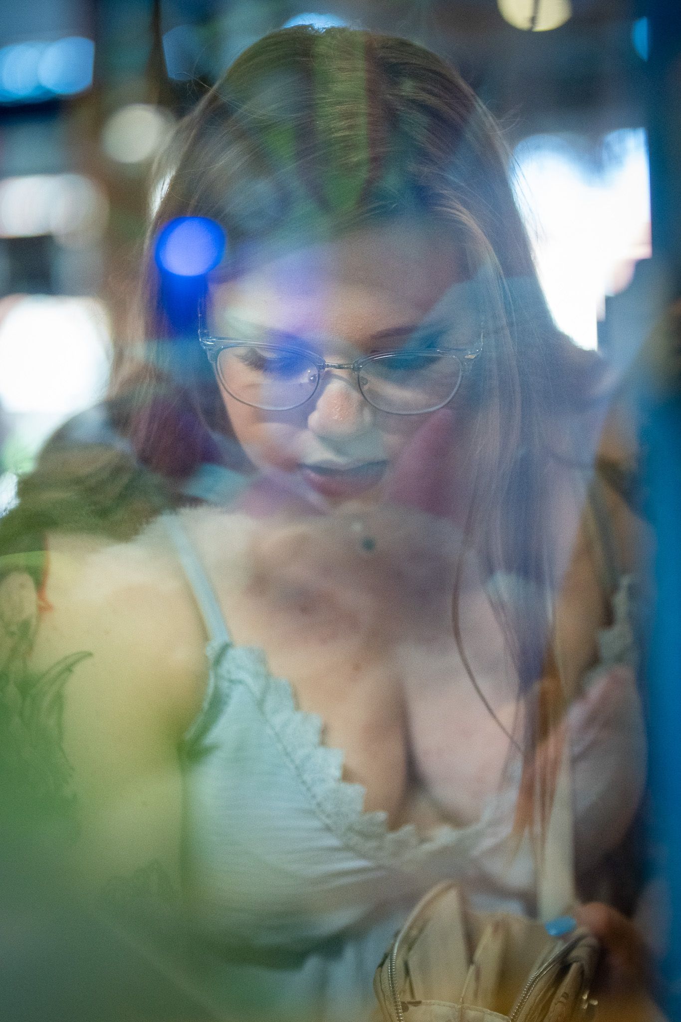 Artistic portrait with soft bokeh lights and reflections showing a figure in glasses and a light top looking downward.