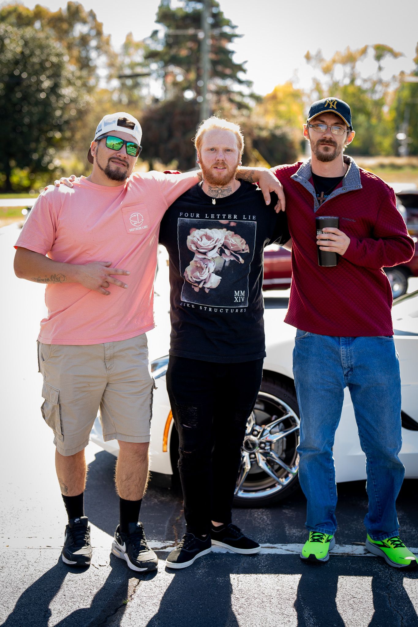 Three men stand together in casual attire casting long shadows on a sunny outdoor pavement.