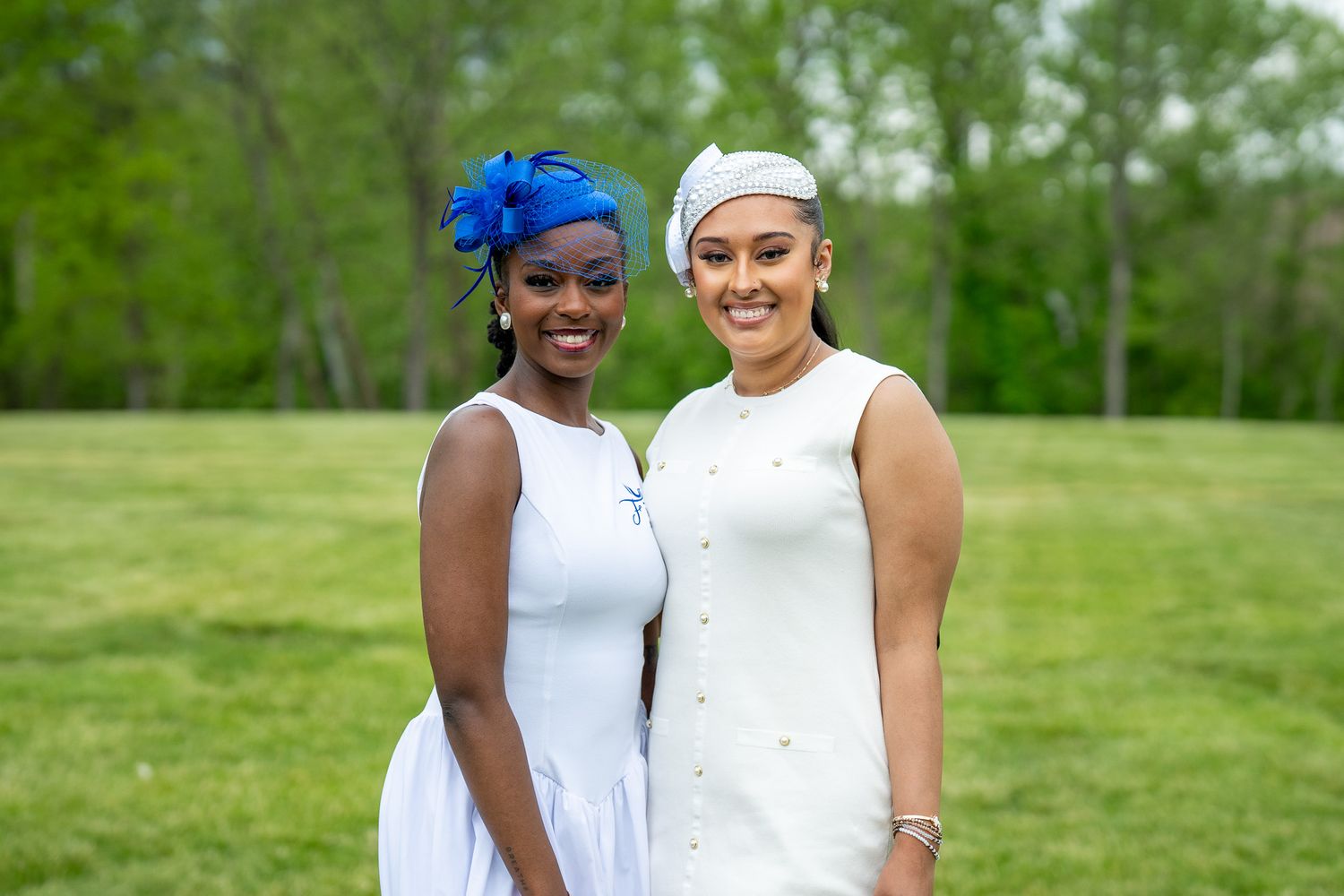 Two tennis players stand close together smiling on an outdoor court surrounded by green trees.