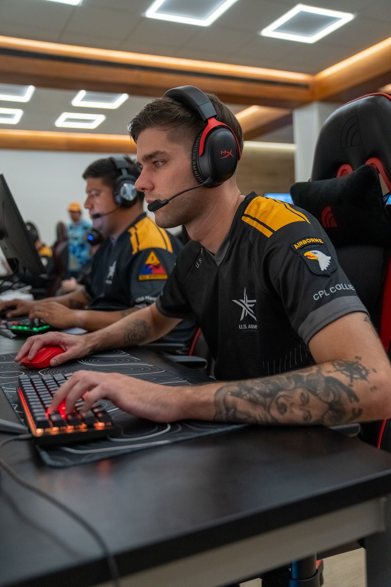 Professional esports players wearing headsets compete at gaming stations during a competitive tournament.