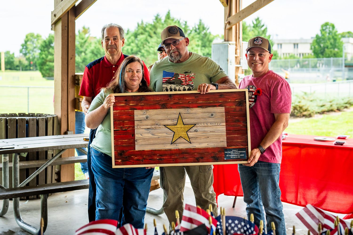 Group displaying rustic wooden plaque with star design at patriotic outdoor gathering.