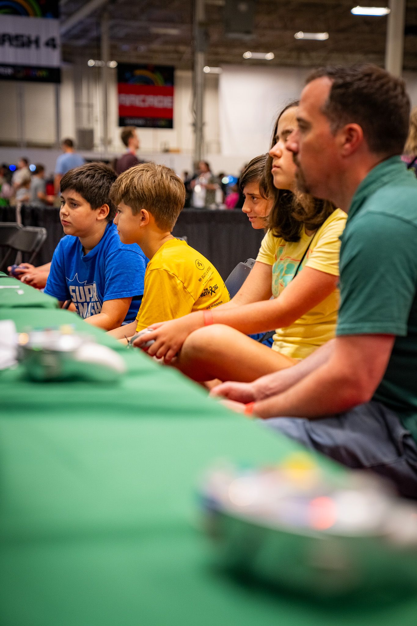 A group of people sitting at a long green gaming table focused intently during a competitive event.