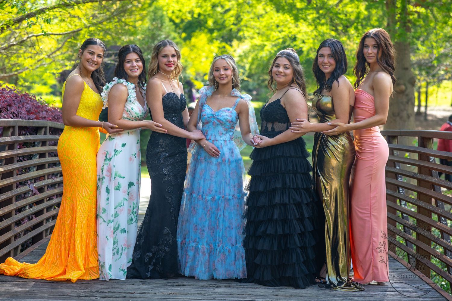 Group of high school girls in colorful prom dresses posing together on a wooden bridge — group senior portraits in York County, SC.