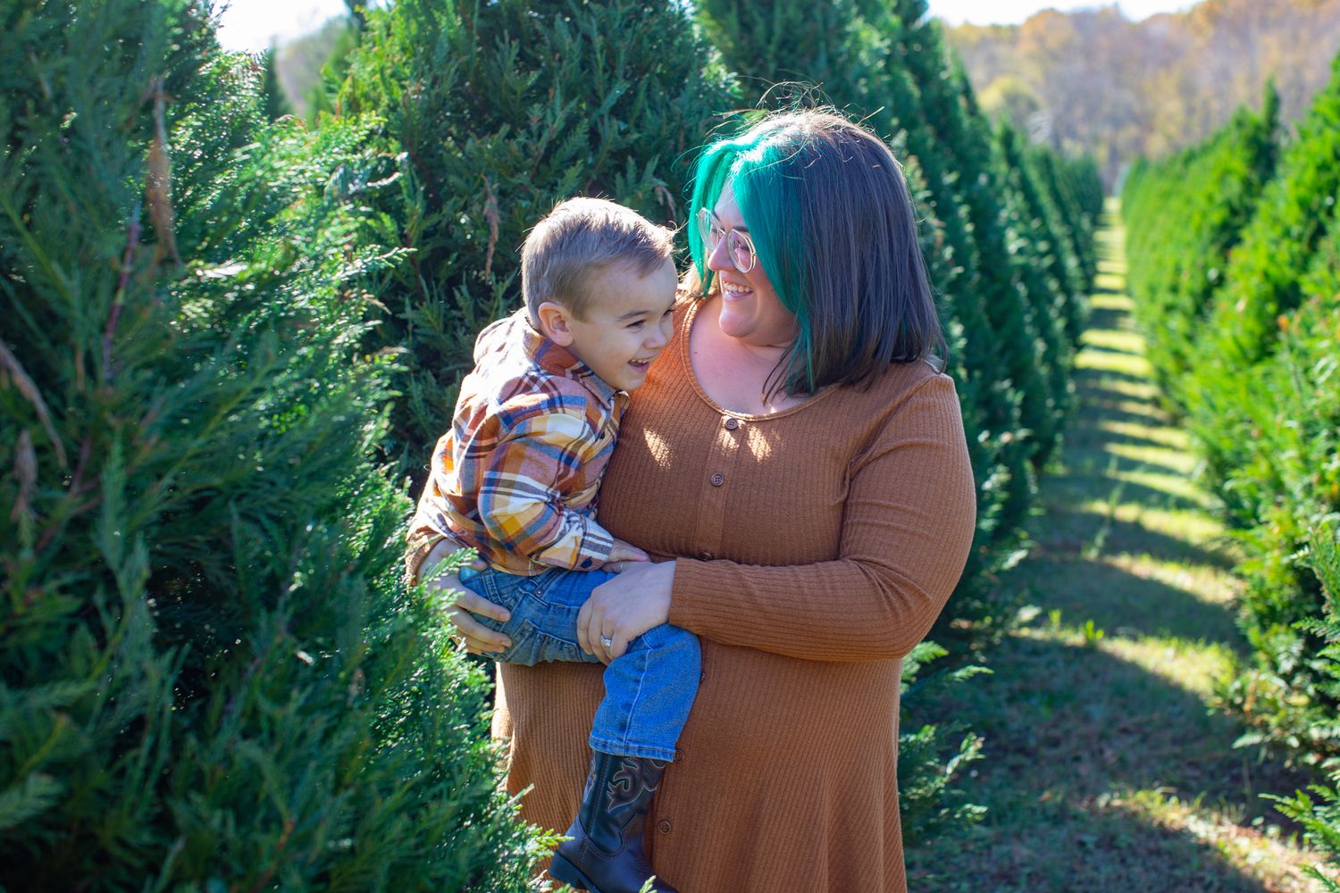 Mother and Son embracing between rows of Christmas trees, wearing cozy winter outfits — holiday portraits in York, SC.