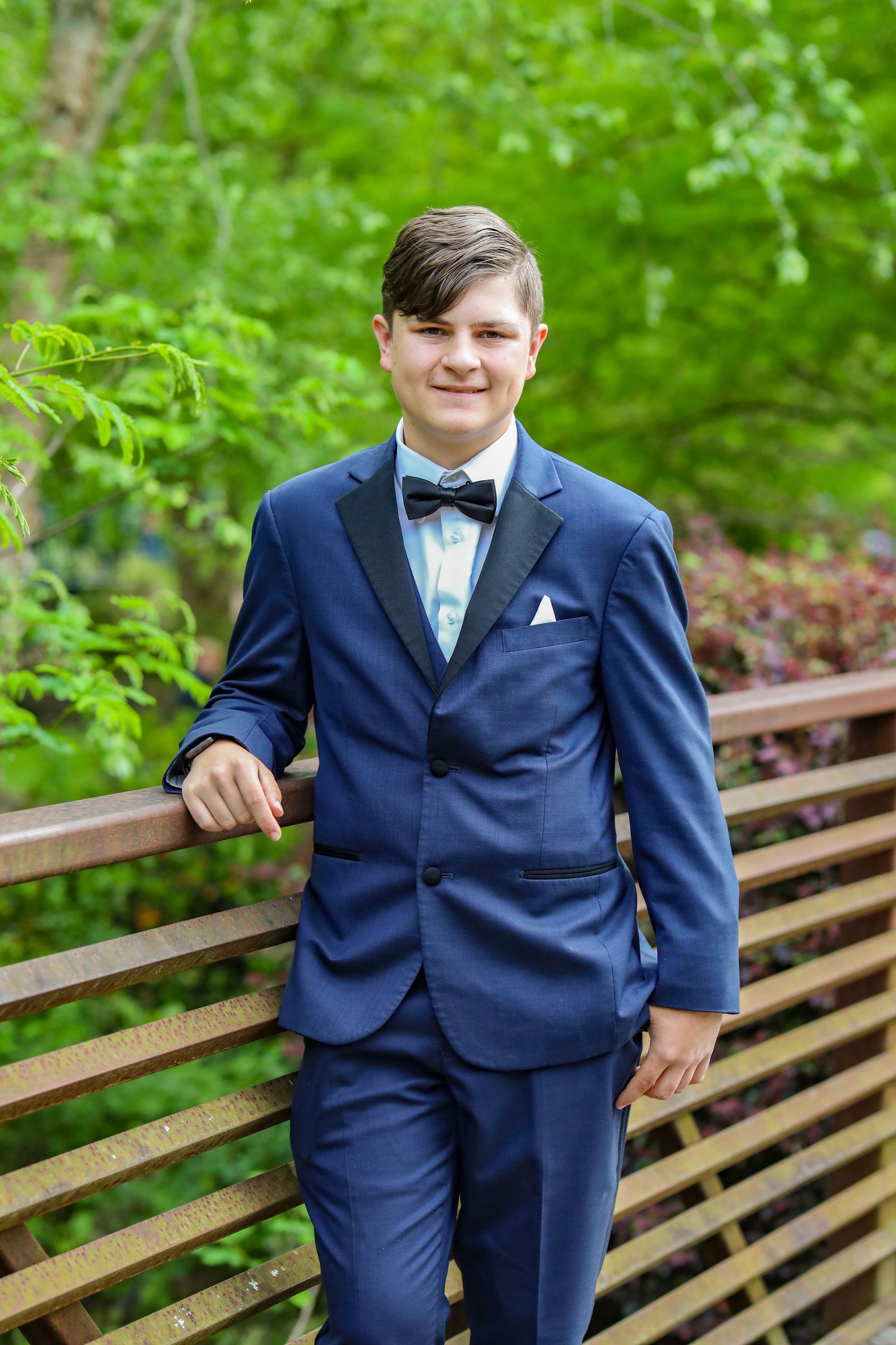 High school senior boy in navy suit and bow tie leaning on wooden bridge railing — formal prom portrait in McConnells, SC.
