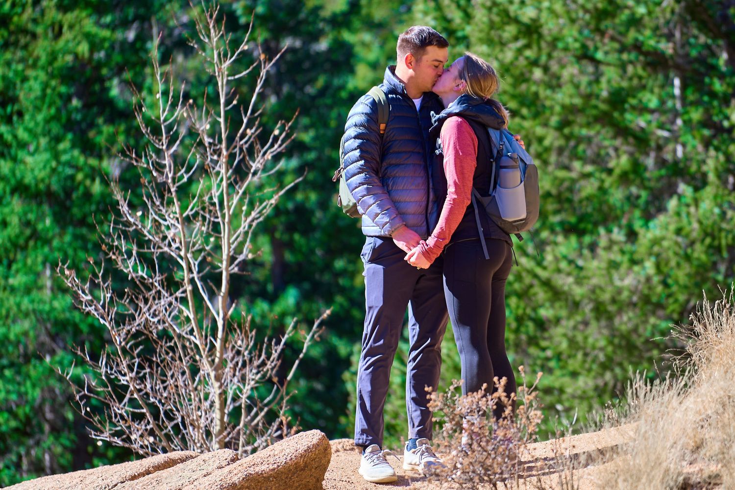 A couple embracing while hiking on a mountain trail surrounded by lush greenery.