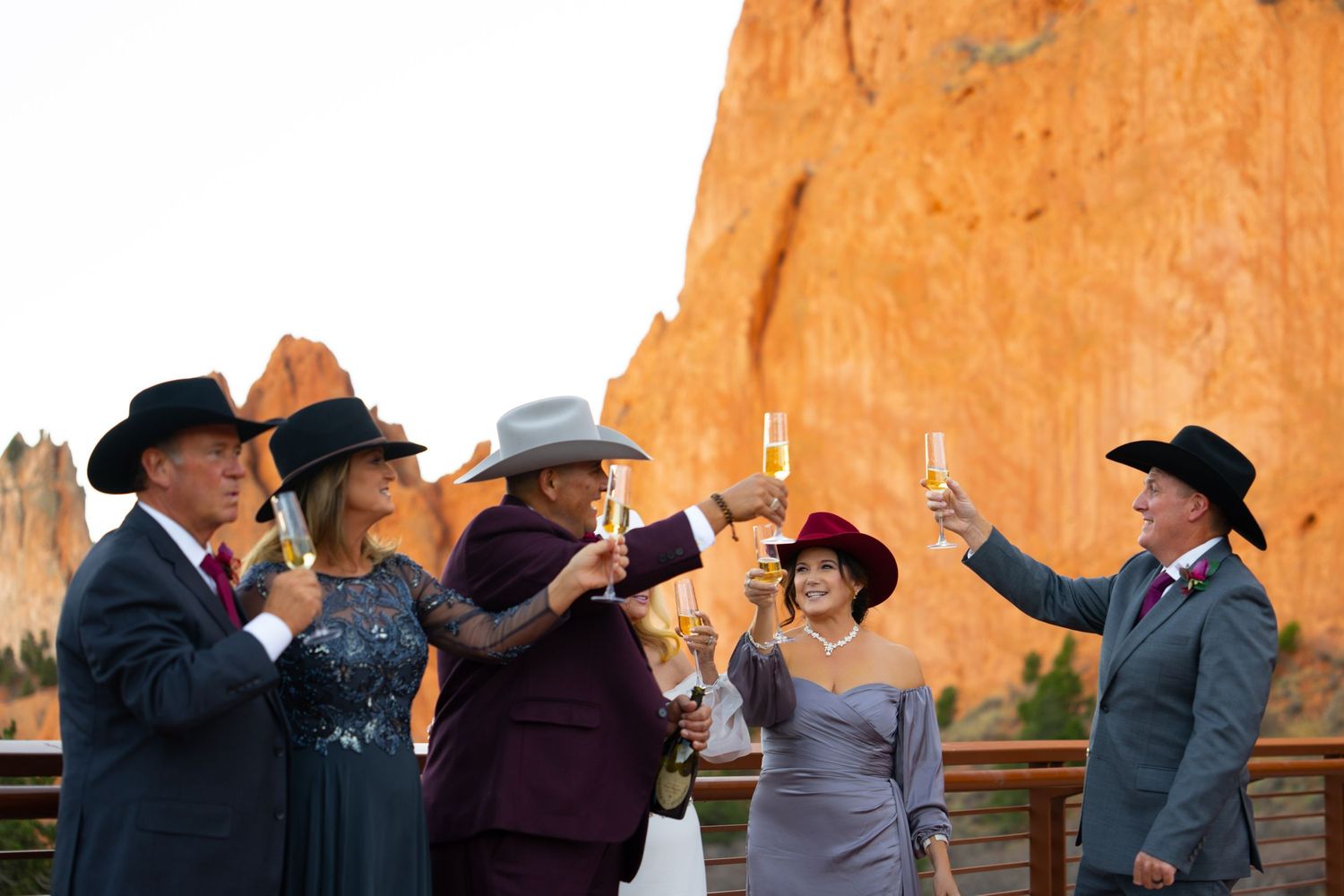 A group of people wearing cowboy hats gather outdoors against a backdrop of red rock formations.