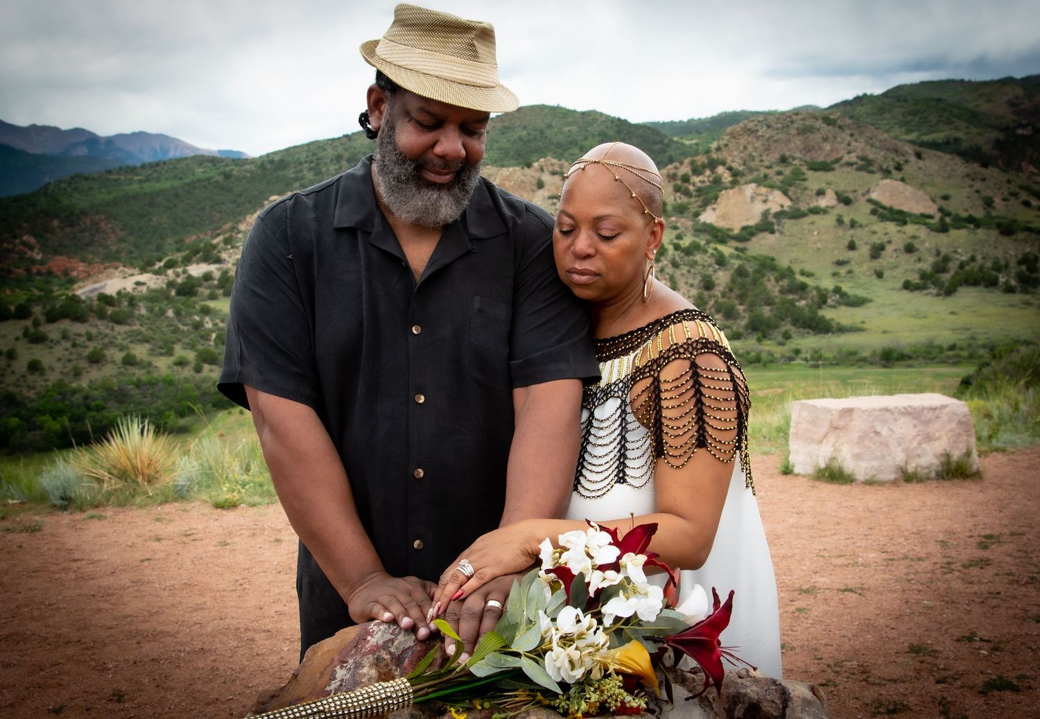 A couple holds a floral bouquet together in a scenic mountain desert landscape.