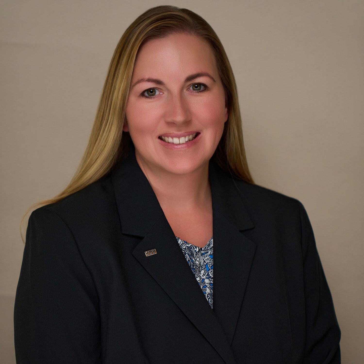 Professional headshot in black blazer against neutral background.