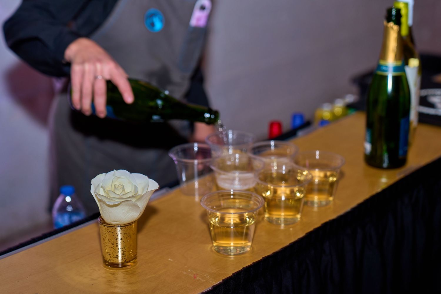Bartender pouring drinks at event with row of shot glasses on counter.