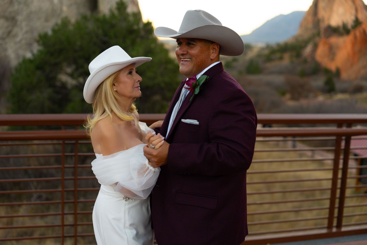 A couple in western wedding attire dance together at sunset against a rustic ranch backdrop.
