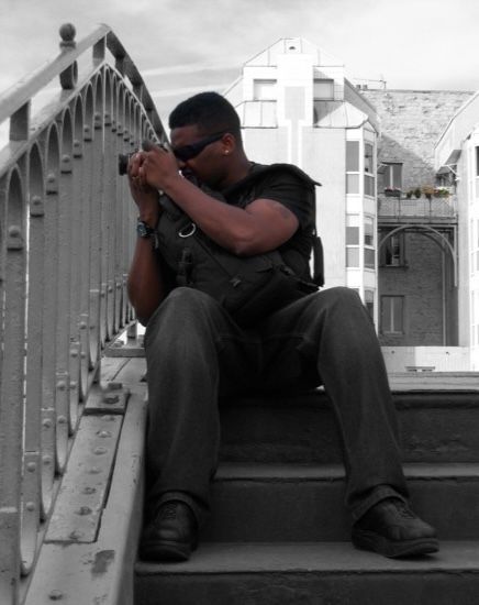 Photographer in tactical gear taking photos from stairway position in monochrome.