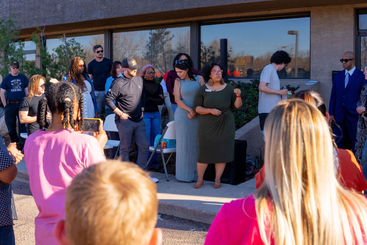 Group of adults gathered outdoors at a community event near a modern building on a sunny day.