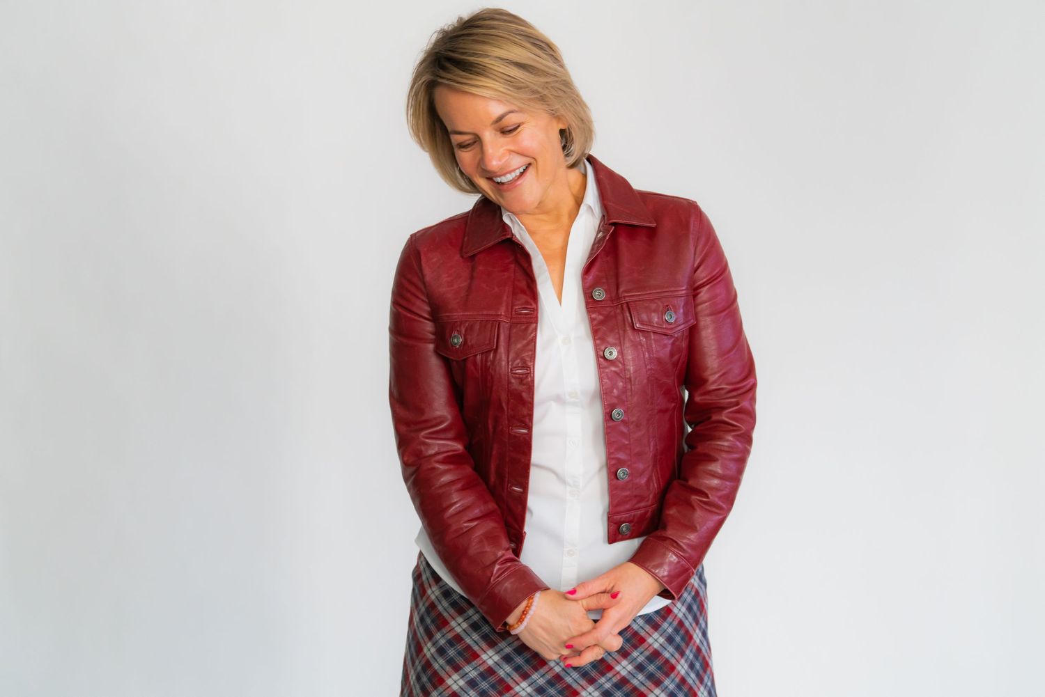 Woman in red leather jacket and plaid skirt poses against white background.