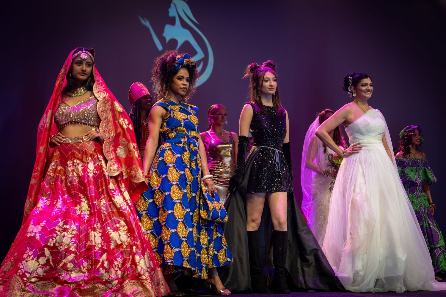 Models walk the runway in vibrant traditional and modern fashion designs at a multicultural fashion show event.