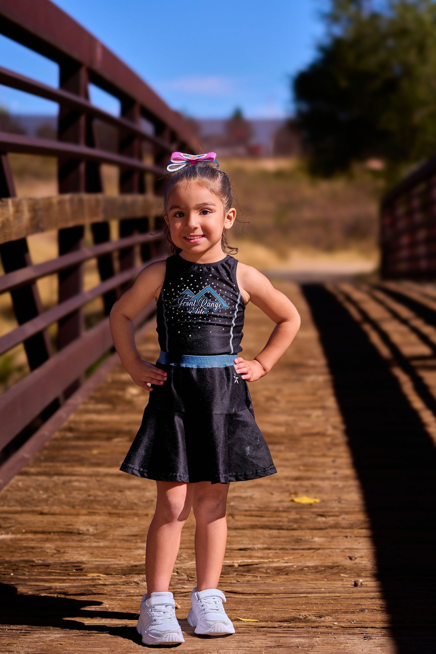 A young dancer in a navy dress strikes a pose on a wooden bridge.