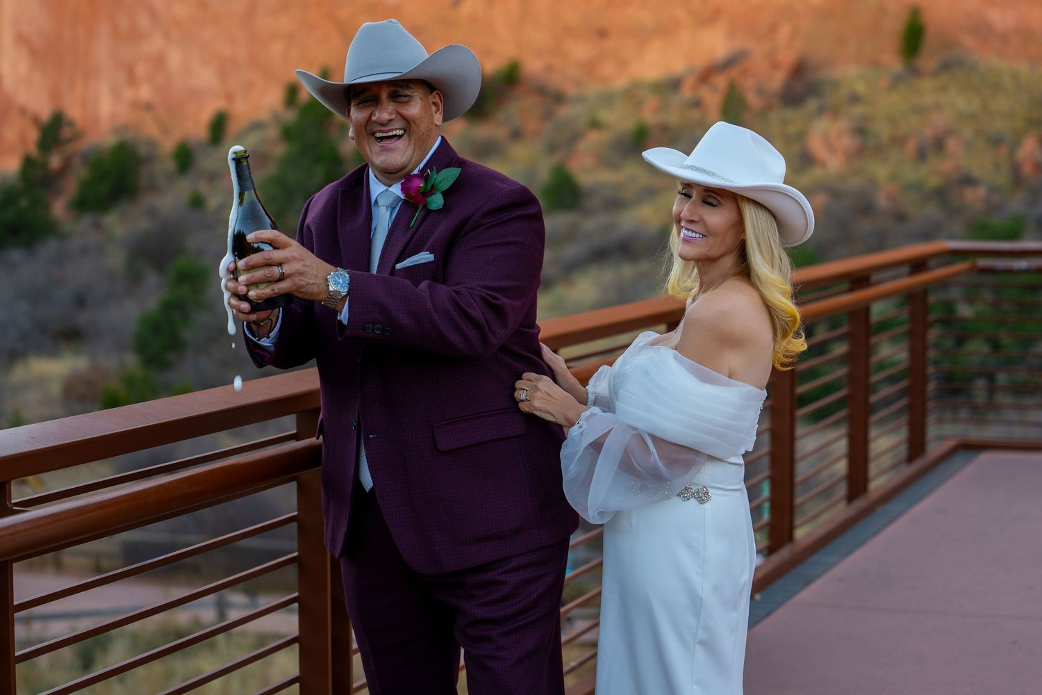Wedding couple and guests gather on a wooden bridge with red rock formations in the background.