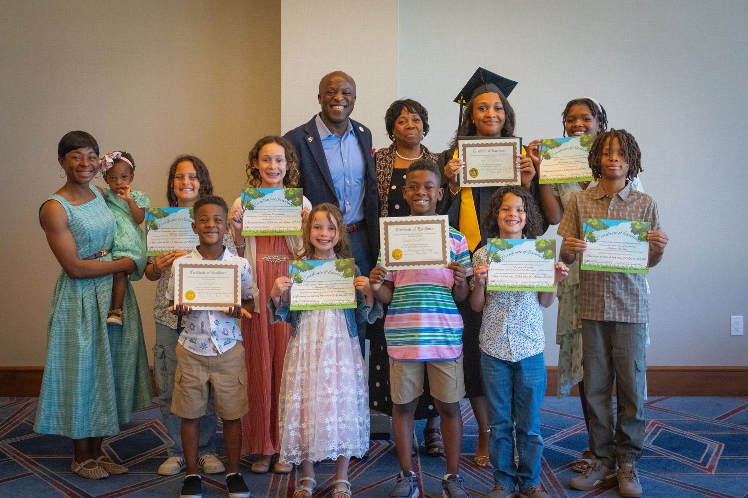 Group of children and adults proudly displaying certificates at an awards ceremony indoors.