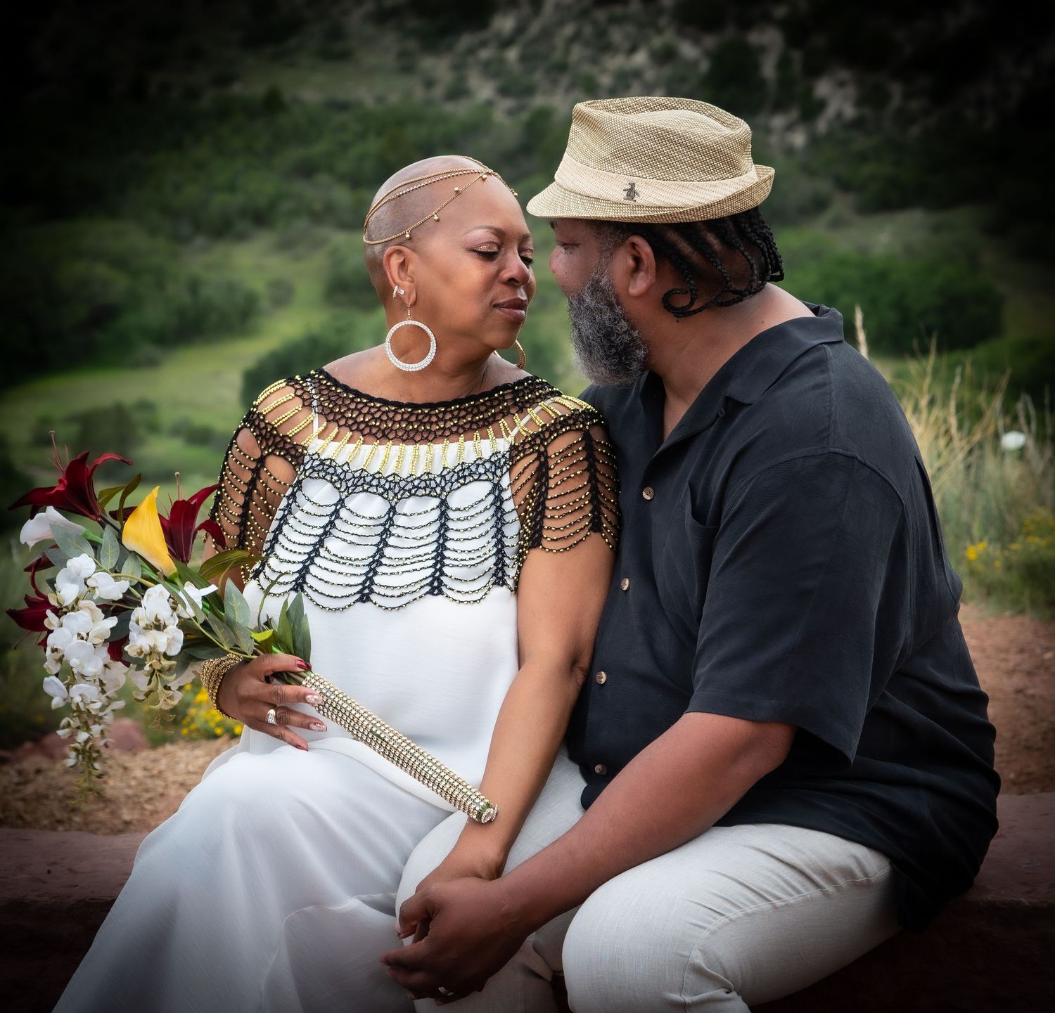 A couple shares an intimate moment in nature while adorned in a white dress and traditional jewelry.
