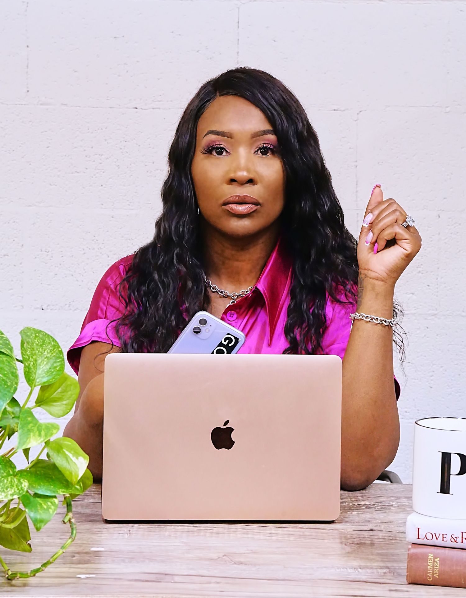 Business professional in pink attire works on laptop with plant and coffee mug on desk.