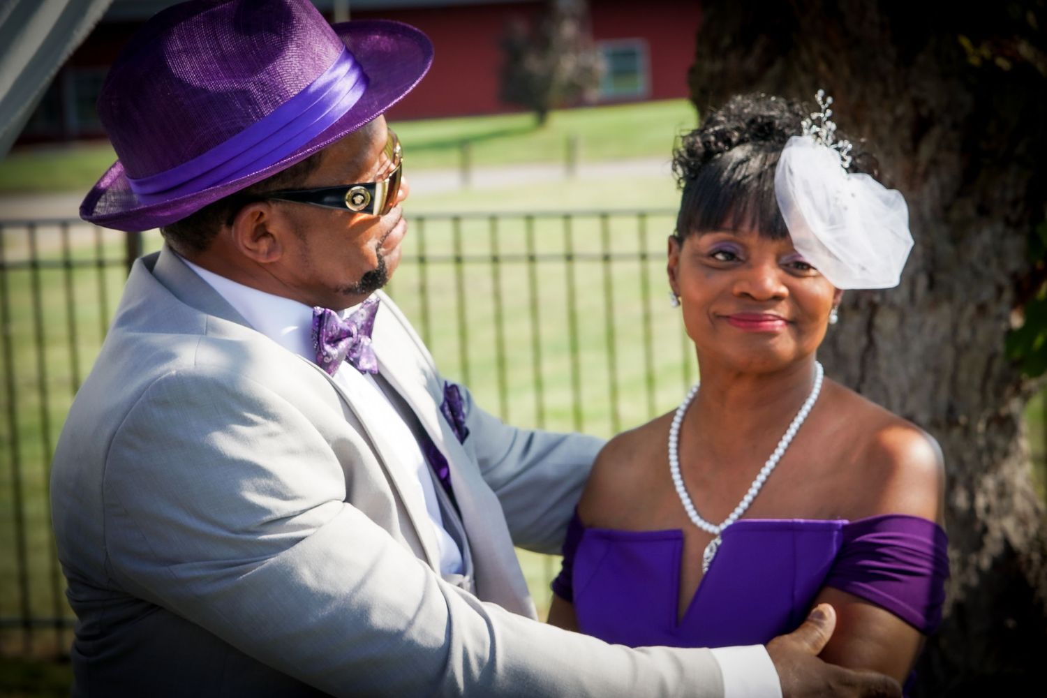 A couple in coordinated purple and white formal attire share a moment at an outdoor event.