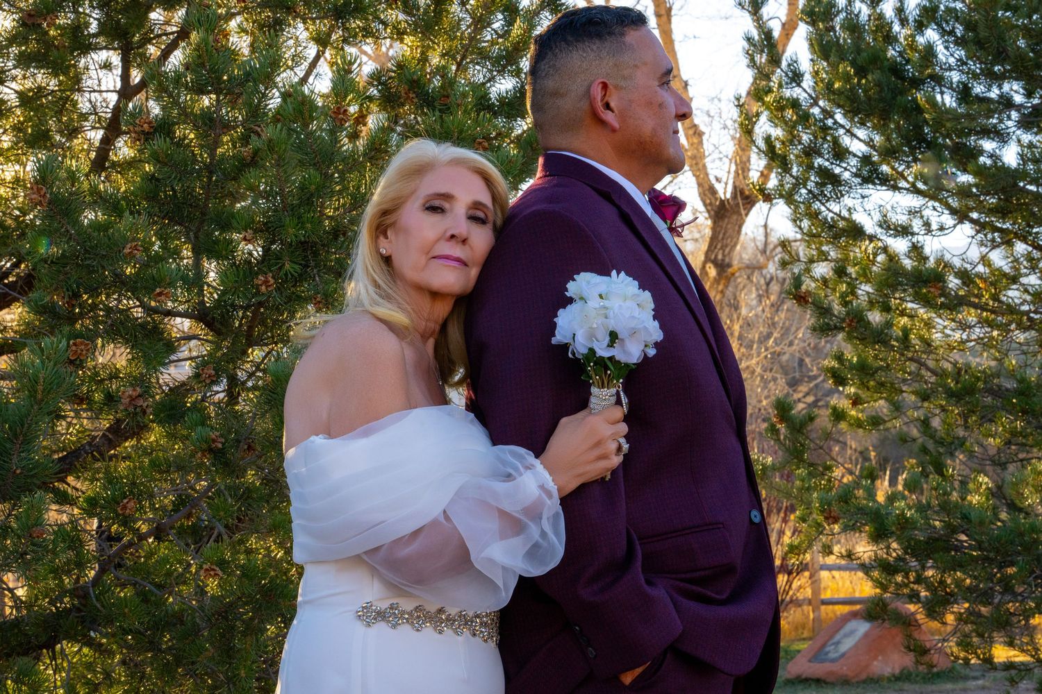 A couple in wedding attire shares a romantic dance outdoors during golden hour surrounded by trees.