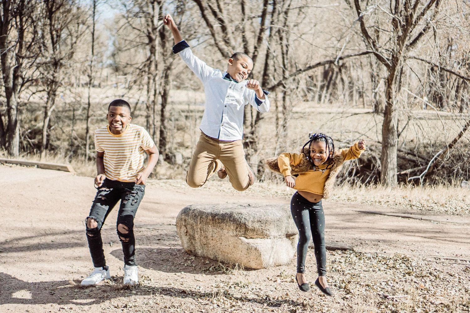 Three people jumping and playing together outdoors in a natural setting.